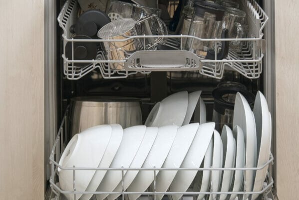 Full loaded Dishwasher machine. Integrated Dishwasher with white plates front vew.