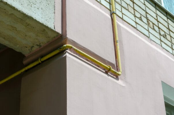 Yellow gas pipe viewed on the outer brick wall of residential building.