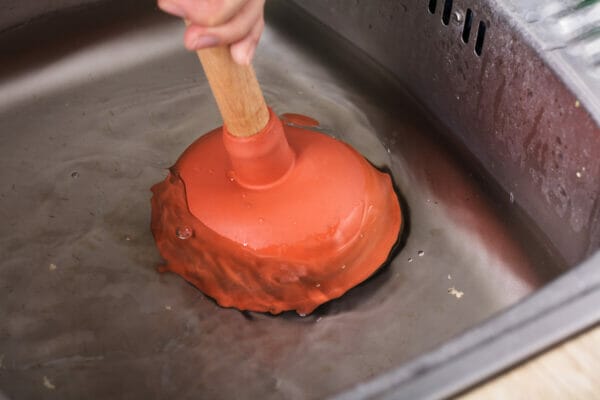 Person Cleaning Sink With Cup Plunger