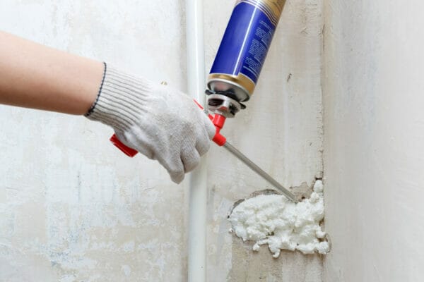 Worker's hand fix a rent in wall using polyurethane foam